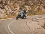 Motociclista en pruebas de motos, inclinado en una curva de carretera montañosa.