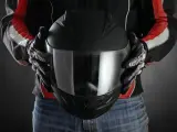 Persona con guantes de moto sostiene casco negro. Se aprecian detalles de las medidas exteriores casco moto en su diseño.