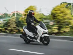 Persona conduce moto blanca con carnet B, disfrutando del paisaje borroso.