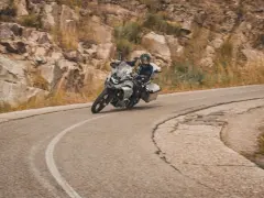 Motociclista en pruebas de motos, inclinado en una curva de carretera montañosa.