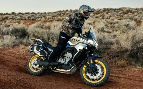 Hombre en moto china trail, recorriendo un camino polvoriento en un paisaje desértico con arbustos secos.