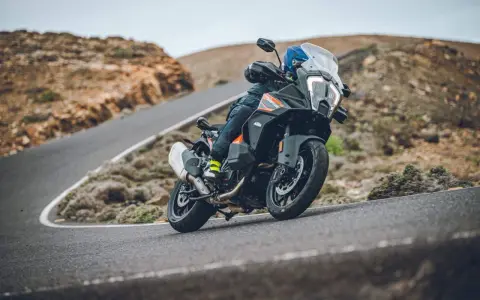 Motociclista en una KTM 1290 Adventure, inclinada en una curva de carretera montañosa. El peso de la moto se siente en la maniobra.