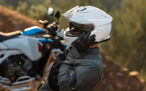Motociclista ajustándose su casco modular silencioso blanco, listo para la aventura.