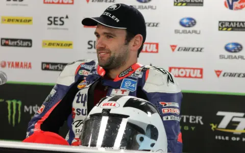 William Dunlop, piloto de motociclismo, sonríe con su casco de carreras y mono de competición.