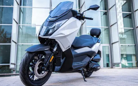 Scooter Mitt 330 GTS blanco y negro, con ABS, aparcado frente a un edificio moderno. ¡Sin problemas para disfrutar!