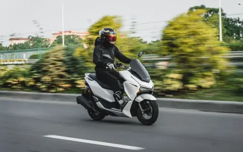 Persona conduce moto blanca con carnet B, disfrutando del paisaje borroso.
