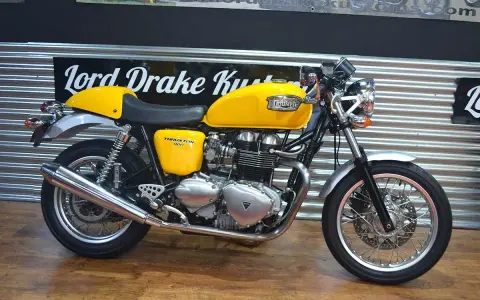 Motocicleta Triumph Thruxton 900 amarilla, estilo café racer, lista para la carretera.