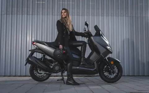 Mujer con casco en mano, sentada en una Wottan Storm T 125 gris. Parece lista para rodar, sin problemas a la vista.