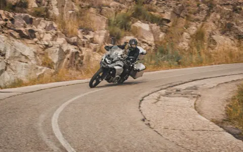 Motociclista en pruebas de motos, inclinado en una curva de carretera montañosa.