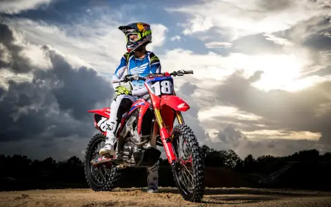 Jett Lawrence, piloto de motocross, posa con su moto roja bajo un cielo dramático.