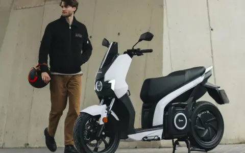 Hombre con casco junto a un scooter eléctrico blanco, el scooter mas potente para la ciudad.