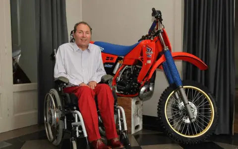Andre Malherbe, leyenda del motocross, sonríe junto a su icónica moto Honda roja.