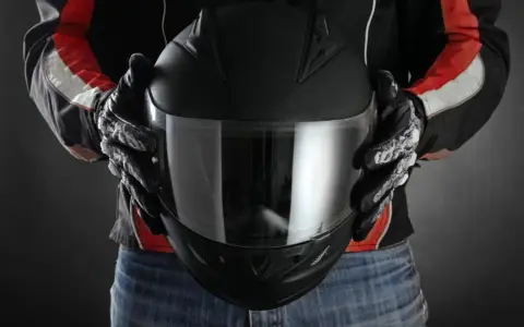 Persona con guantes de moto sostiene casco negro. Se aprecian detalles de las medidas exteriores casco moto en su diseño.