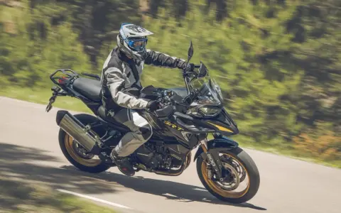 Motociclista con equipo de protección conduce una de las motos trail media cilindrada por una carretera rodeada de vegetación.