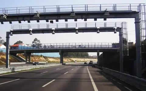 Un pórtico de peaje automático en España. Los coches circulan por la autopista bajo una estructura metálica con antenas.