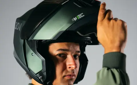 Hombre ajustando su casco integral o modular, de color verde militar, con sistema de ventilación.