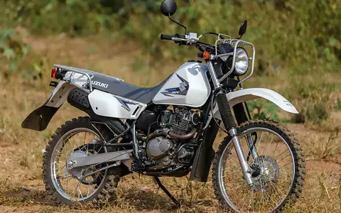 Suzuki DR 200 lista para la aventura. Moto blanca de doble propósito con neumáticos todoterreno, lista para explorar caminos rurales.
