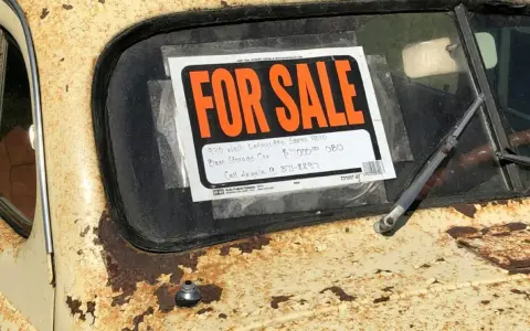 Coche antiguo a la venta, con cartel "FOR SALE". Para saber si una moto tiene cargas, revisa su historial.