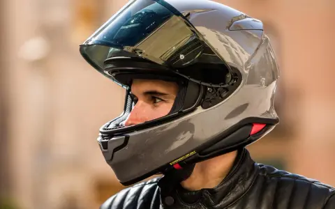 Hombre con casco de moto gris brillante. ¿Cuánto pesa un casco de moto? Este modelo parece ligero y aerodinámico.