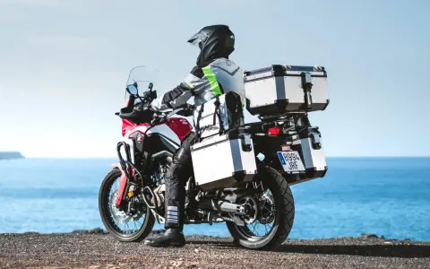 Motociclista con equipaje de **marca Kappa** listo para la aventura junto al mar.