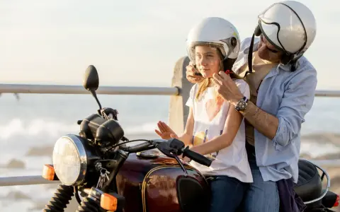 Un hombre ajusta el casco a un niño en una moto, listos para una aventura junto al mar.