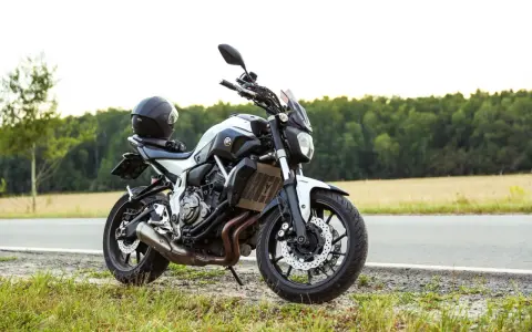 Una moto a2 blanca y negra, con un casco negro en el asiento, aparcada en la cuneta de una carretera rural.