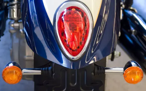 Detalle de la parte trasera de una moto azul y blanca, con intermitentes naranjas y luz roja. Podría ser una multa por llevar luces led moto.