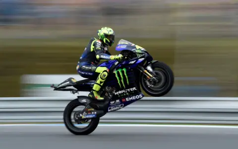 Valentino Rossi levanta la rueda trasera de su Yamaha en plena carrera, con su icónico casco amarillo y traje azul.