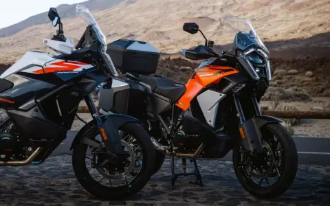 Dos motos KTM Super Adventure listas para la aventura. Modelos naranjas y blancos, con maletas, en un paisaje árido.