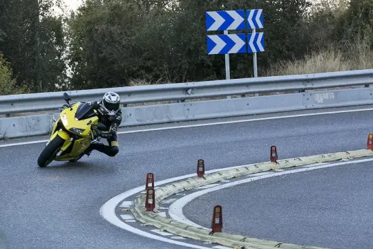 Motociclista inclinado en una curva cerrada en la carretera de la Rabassada, con señales de advertencia y barreras de seguridad.