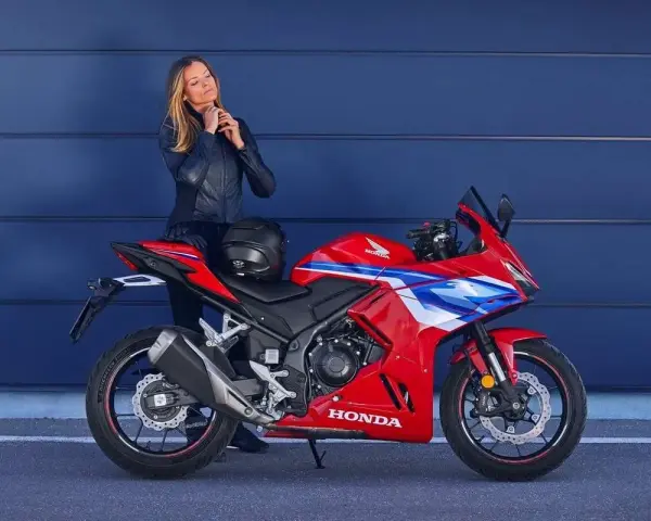 Mujer con chaqueta de cuero junto a una moto deportiva roja Honda. Ideal para quienes buscan motos tetracilindricas a2.