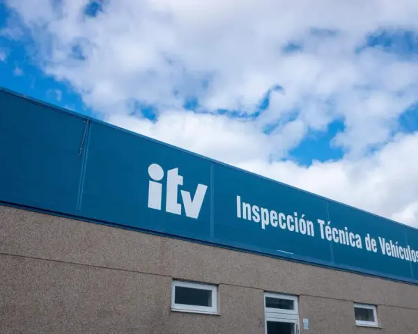 Edificio de la ITV bajo un cielo azul con nubes. El letrero blanco dice "itv Inspección Técnica de Vehículos".