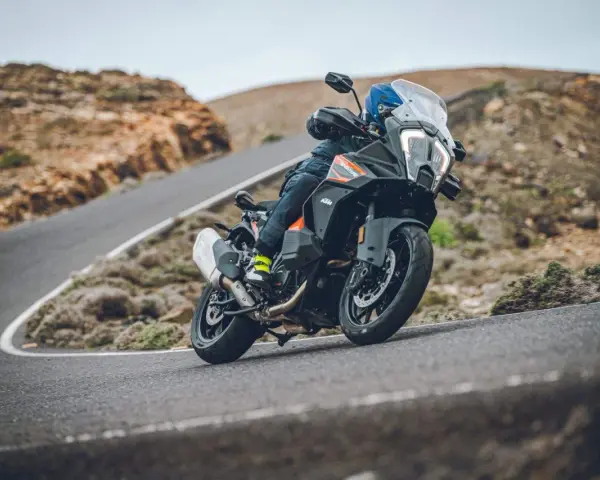 Motociclista en una KTM 1290 Adventure, inclinada en una curva de carretera montañosa. El peso de la moto se siente en la maniobra.