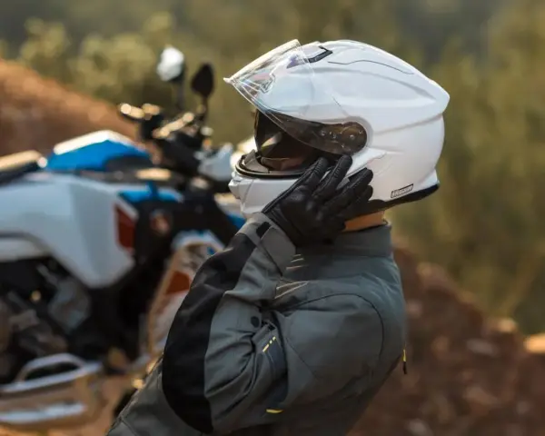 Motociclista ajustándose su casco modular silencioso blanco, listo para la aventura.