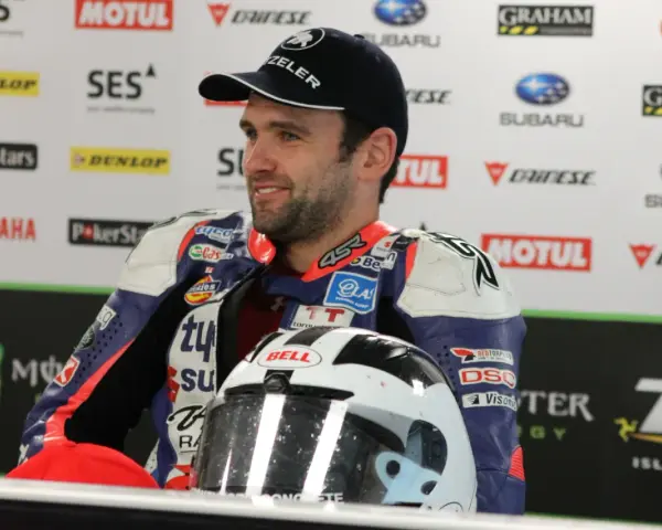 William Dunlop, piloto de motociclismo, sonríe con su casco de carreras y mono de competición.