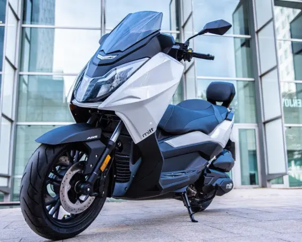 Scooter Mitt 330 GTS blanco y negro, con ABS, aparcado frente a un edificio moderno. ¡Sin problemas para disfrutar!