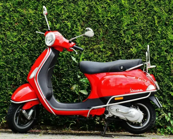 Scooter roja aparcada frente a un seto verde. Ideal para entender las diferencias carnet a1 y a2.