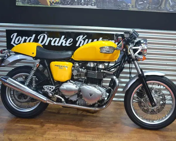 Motocicleta Triumph Thruxton 900 amarilla, estilo café racer, lista para la carretera.