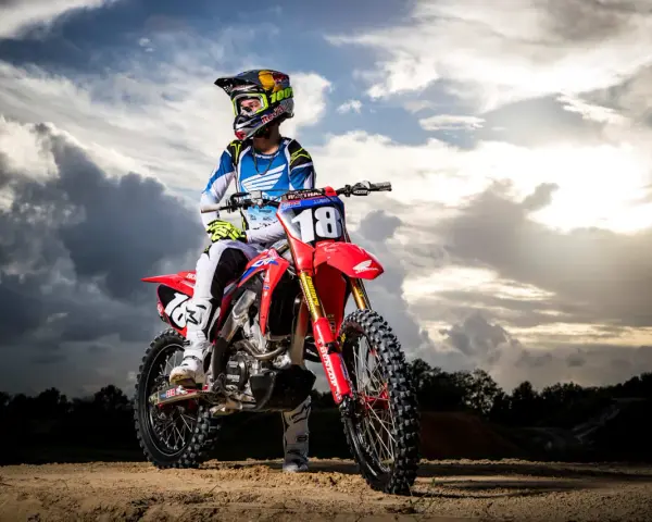 Jett Lawrence, piloto de motocross, posa con su moto roja bajo un cielo dramático.
