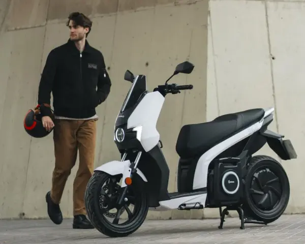 Hombre con casco junto a un scooter eléctrico blanco, el scooter mas potente para la ciudad.