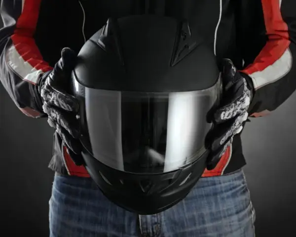 Persona con guantes de moto sostiene casco negro. Se aprecian detalles de las medidas exteriores casco moto en su diseño.