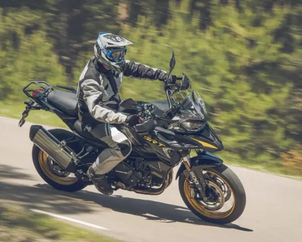 Motociclista con equipo de protección conduce una de las motos trail media cilindrada por una carretera rodeada de vegetación.