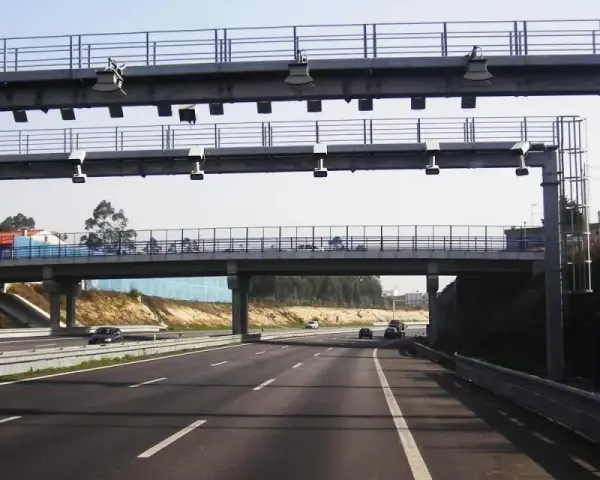 Un pórtico de peaje automático en España. Los coches circulan por la autopista bajo una estructura metálica con antenas.