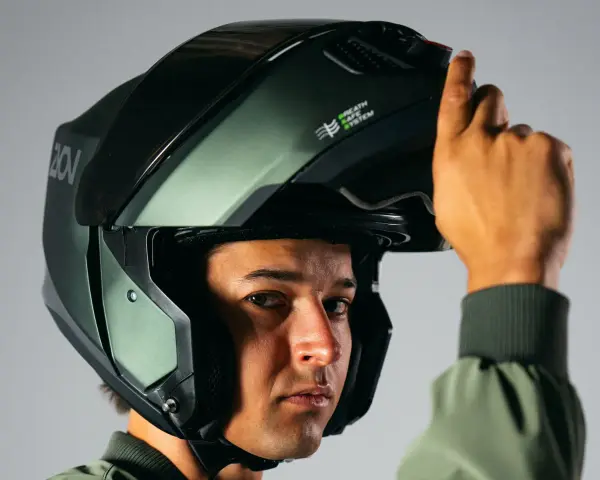 Hombre ajustando su casco integral o modular, de color verde militar, con sistema de ventilación.