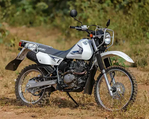 Suzuki DR 200 lista para la aventura. Moto blanca de doble propósito con neumáticos todoterreno, lista para explorar caminos rurales.