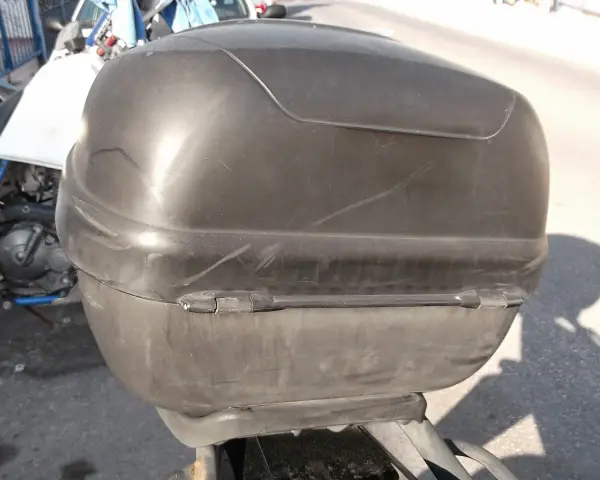 Baúl negro de moto, con marcas de uso. ¿Será que alguien pensó en pintar el baúl de la moto para darle un nuevo look?