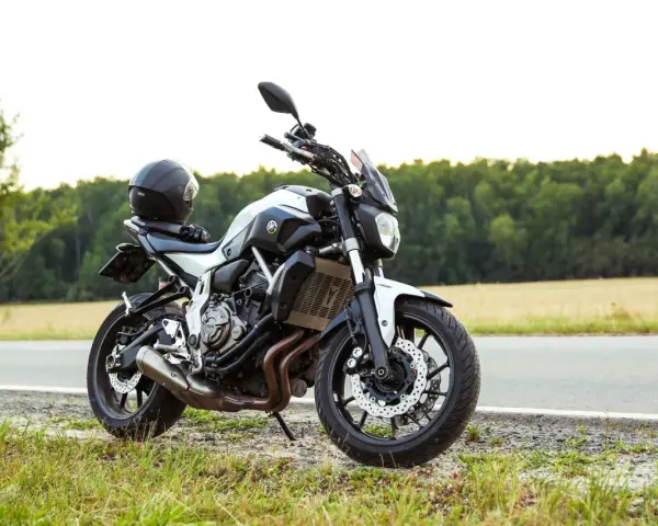 Una moto a2 blanca y negra, con un casco negro en el asiento, aparcada en la cuneta de una carretera rural.