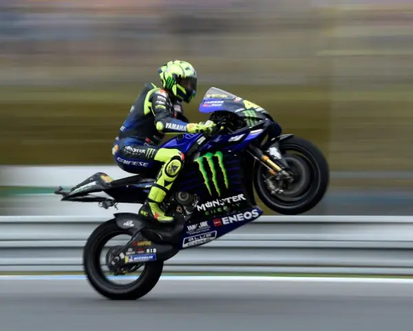 Valentino Rossi levanta la rueda trasera de su Yamaha en plena carrera, con su icónico casco amarillo y traje azul.