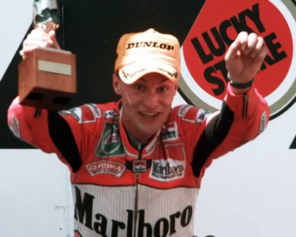 Ralf Waldmann, piloto de motos, celebra con un trofeo y un puño en alto, luciendo su traje de competición Marlboro.