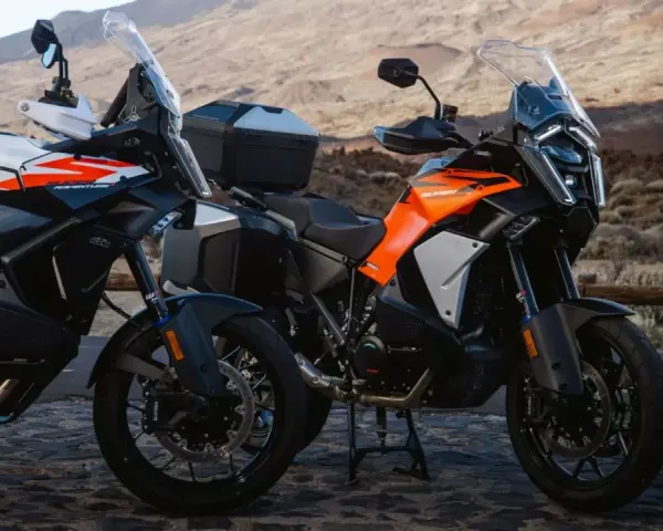 Dos motos KTM Super Adventure listas para la aventura. Modelos naranjas y blancos, con maletas, en un paisaje árido.